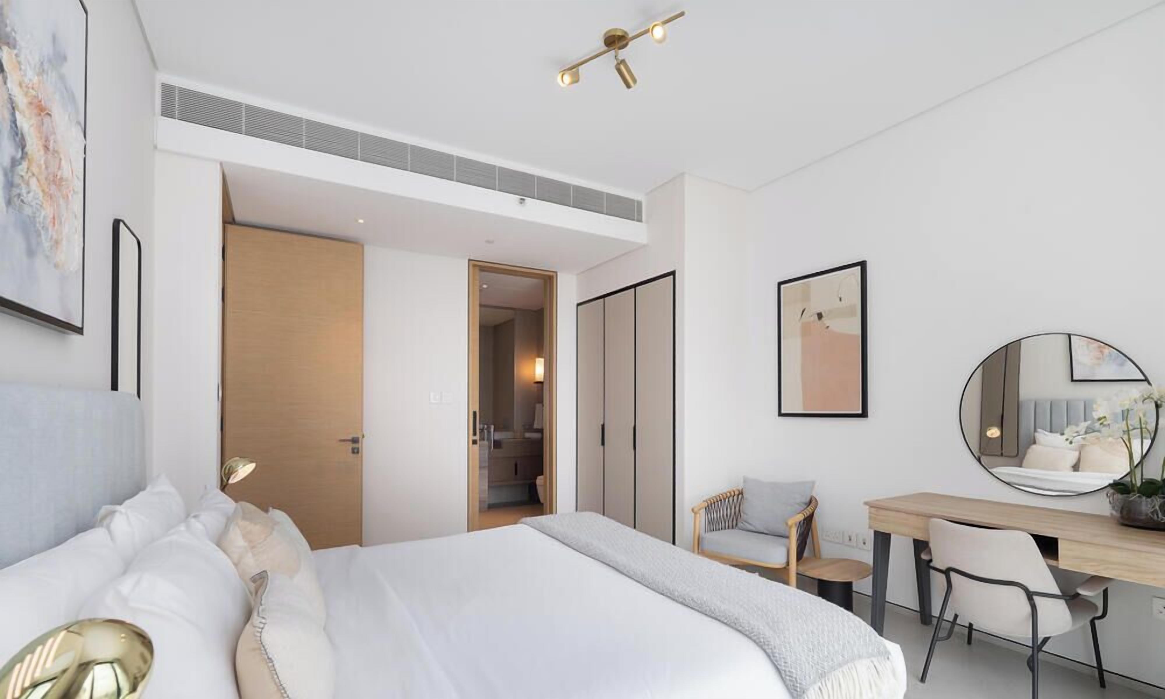 A modern bedroom with a bed, a desk, a chair, and a mirror.