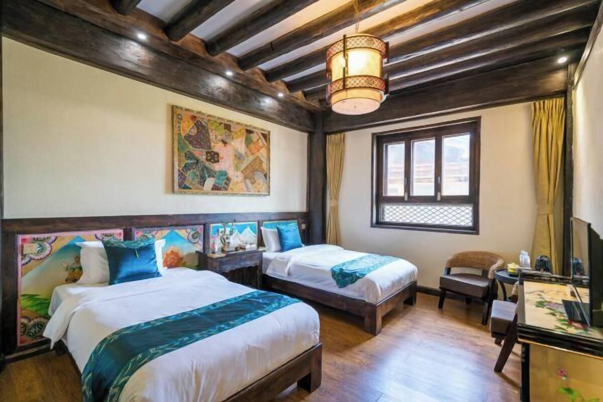 Une chambre avec deux lits, un bureau, une chaise, une fenêtre donnant sur un beau paysage et un tableau au mur.