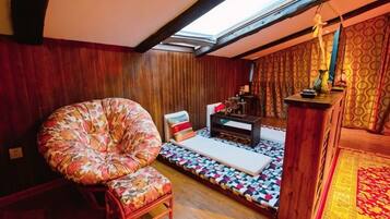A cozy room with a wooden ceiling, a large floral chair, a small table, and a patterned rug.