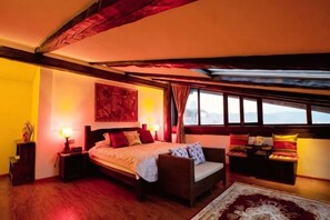 Une chambre avec un grand lit, une fenêtre avec des rideaux, une table de chevet et une œuvre d’art accrochée au mur.