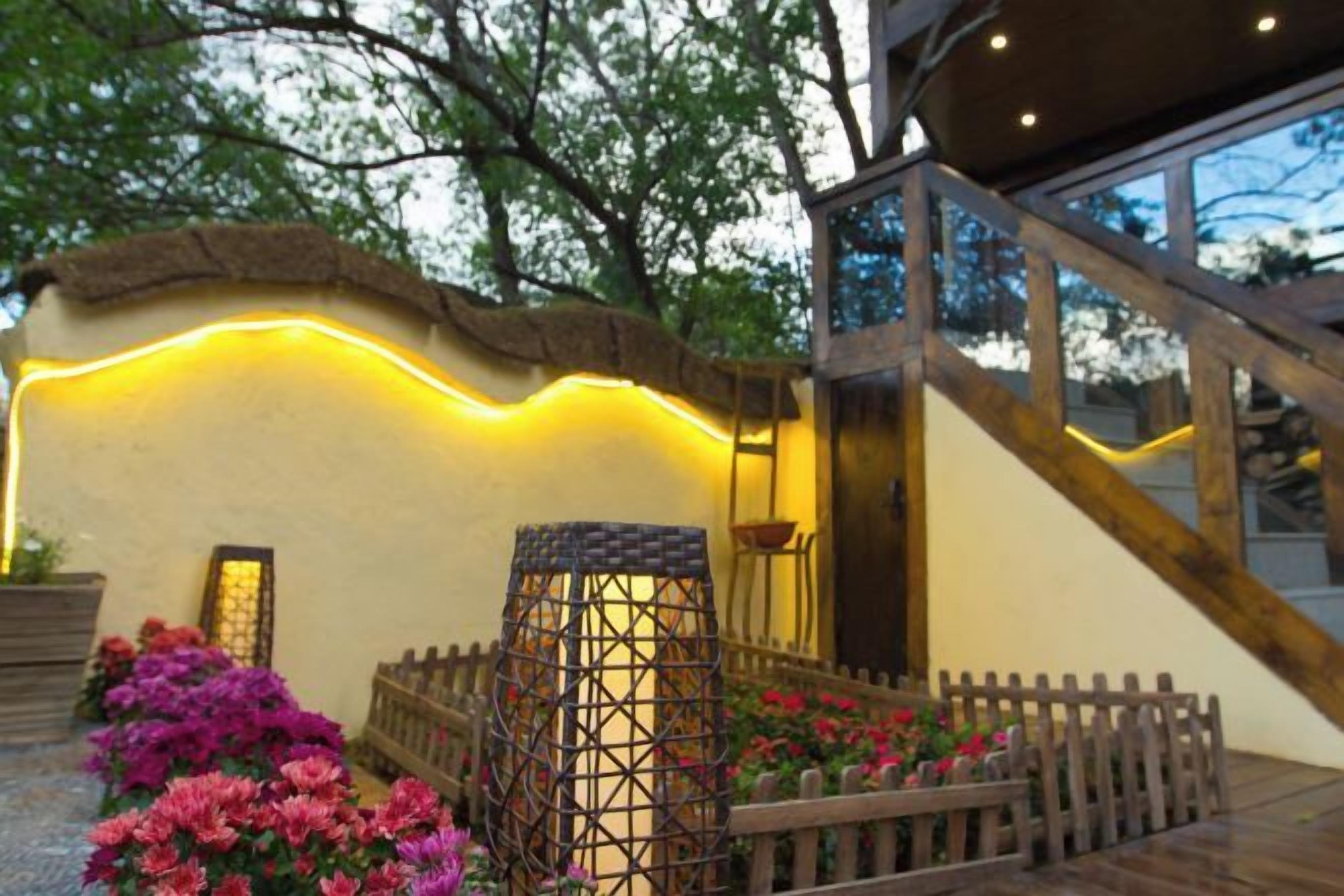 A building exterior with a wooden staircase, a wall with a curved design, and a garden area with flowers and a decorative lantern.