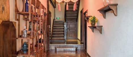 Una escalera de madera que conduce a una puerta, flanqueada por estantes con varios objetos y una lámpara colgante.