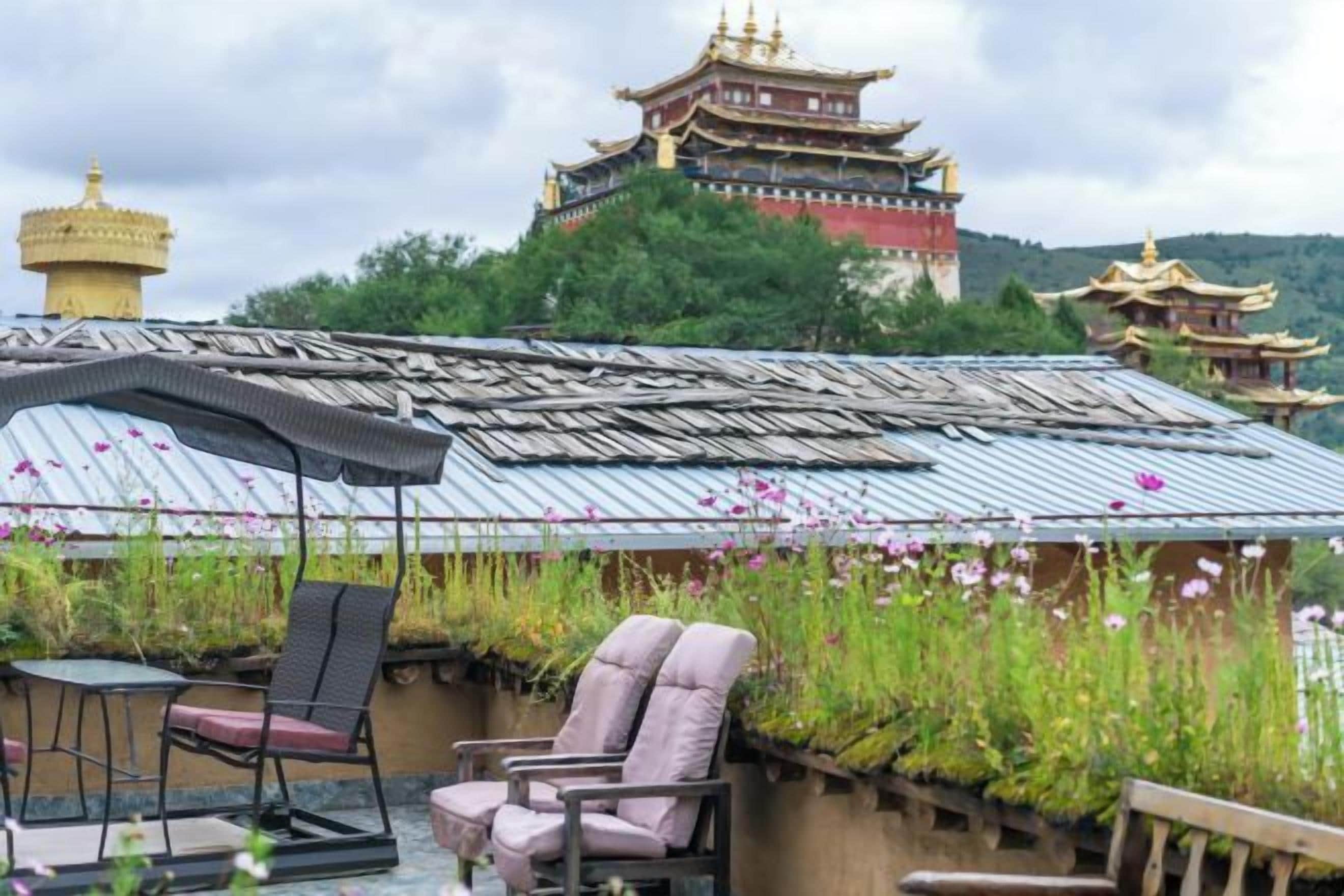 Un edificio tradizionale con tetto in tegole, circondato da vegetazione lussureggiante e con vista su una struttura in stile pagoda sullo sfondo.