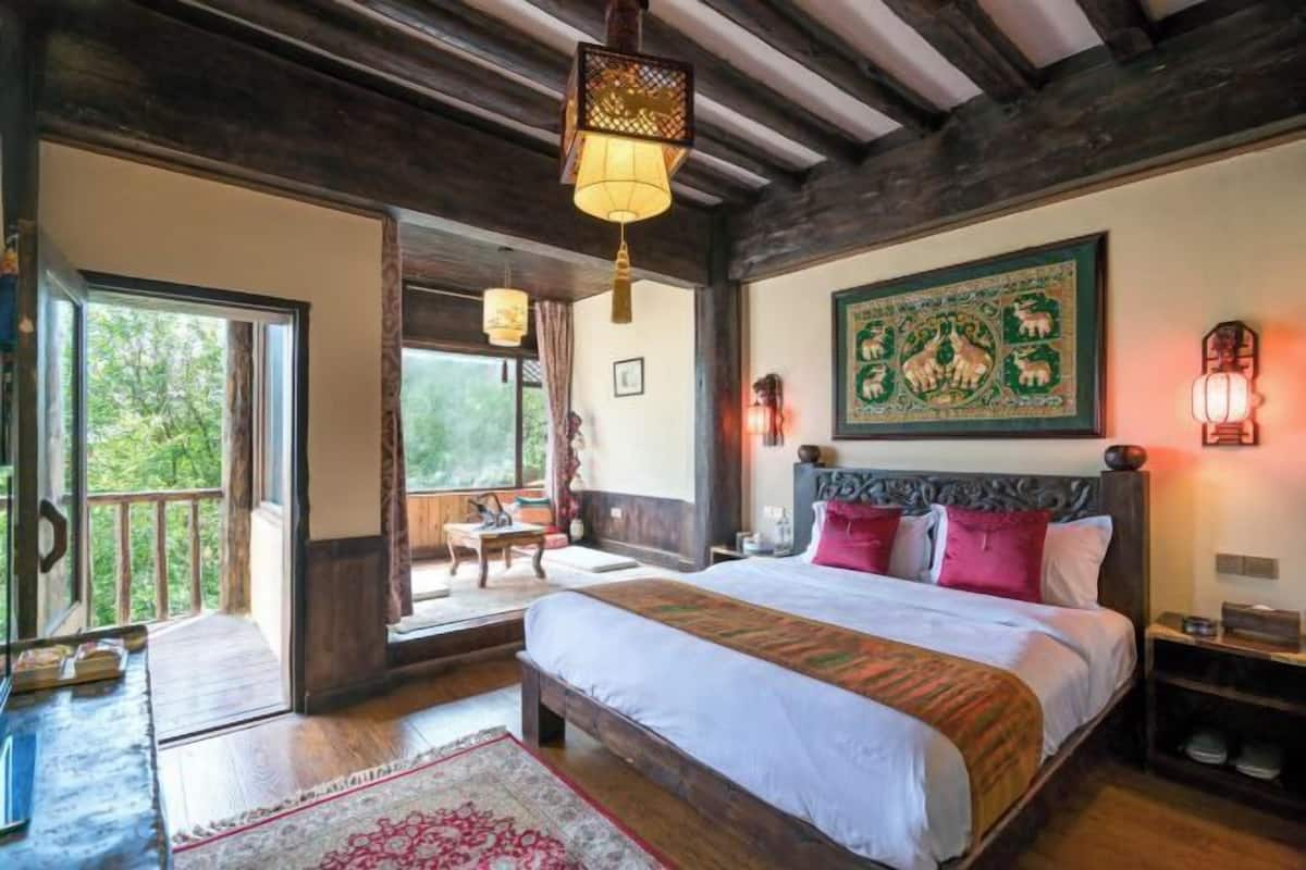 Une chambre avec un grand lit, un plafond en bois, une vue à travers une porte vitrée et une décoration murale traditionnelle.