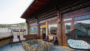Um edifício de madeira com varanda, uma mesa de vidro e uma cadeira suspensa.