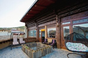 Un bâtiment en bois doté d’un balcon, d’une table en verre et d’un fauteuil suspendu.