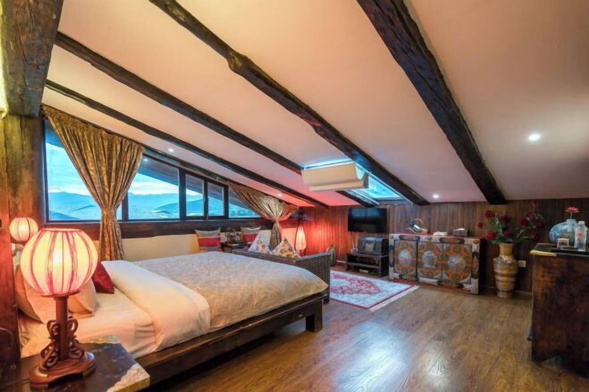 Une chambre à coucher avec un lit, un bureau, une télévision et une fenêtre avec des rideaux.
