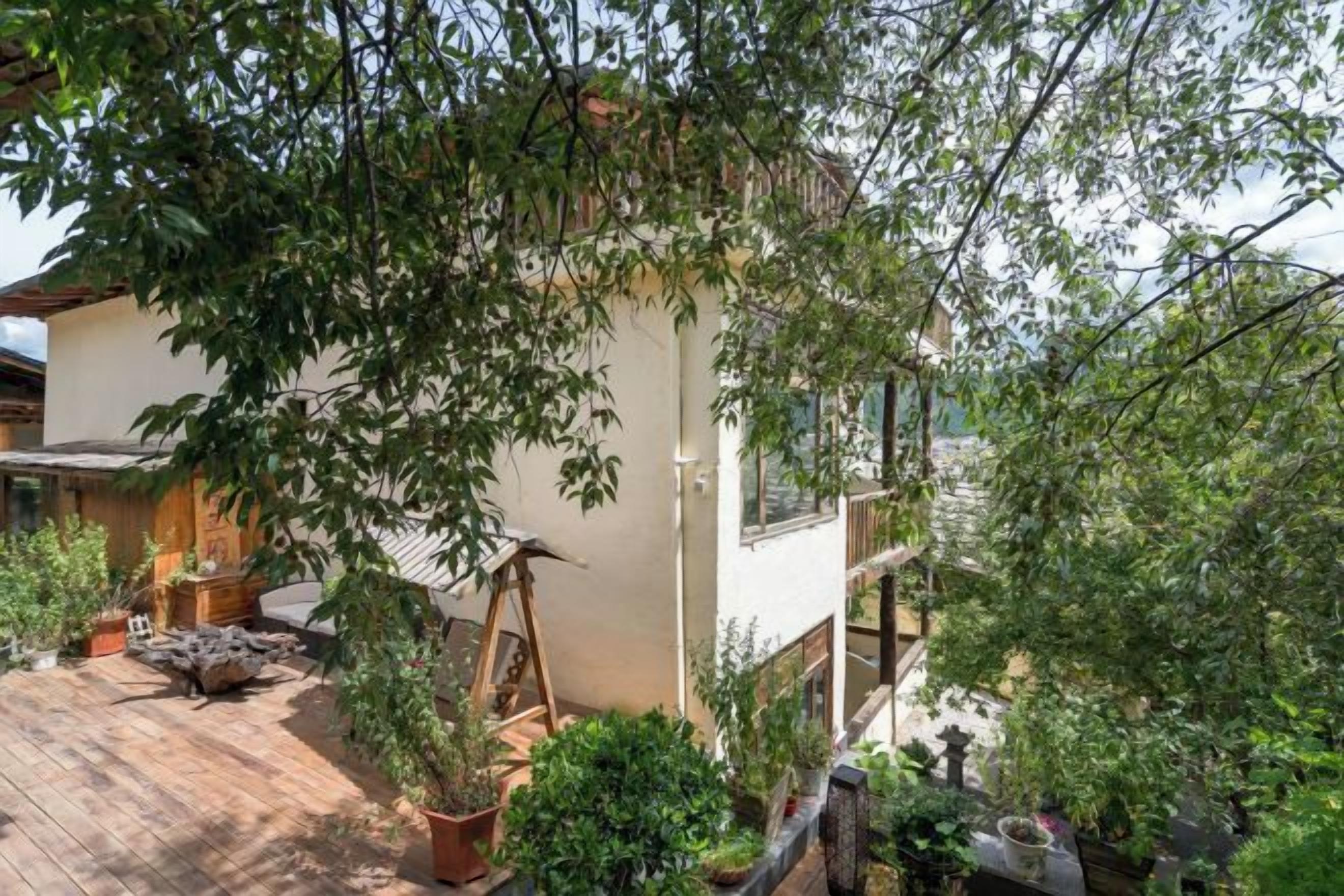 A wooden deck with potted plants, a swing, and a white building with a balcony.