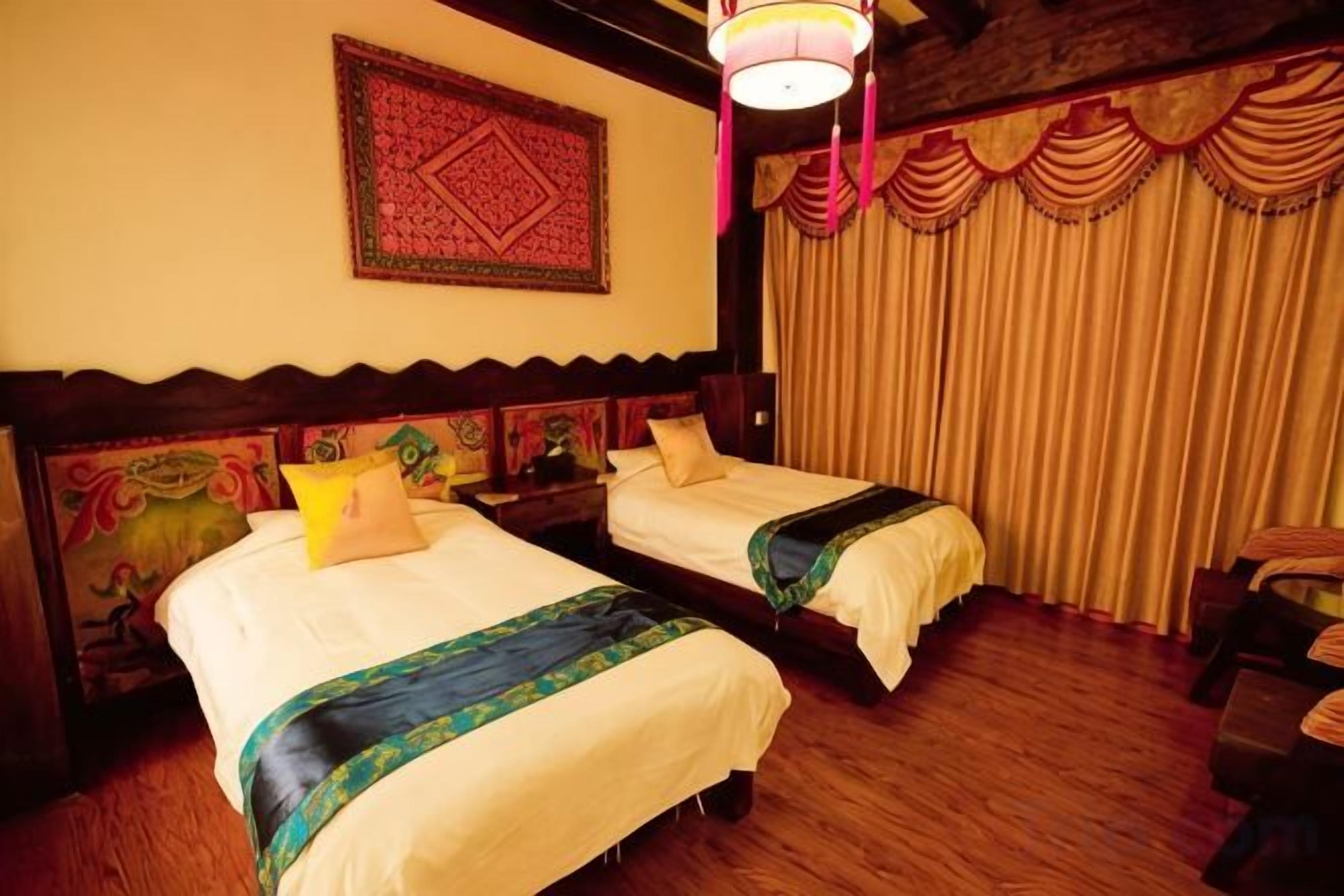 A room with two beds, wooden flooring, a patterned tapestry, and a curtain.