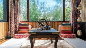 A room with a wooden table, two cushioned benches, a window with curtains, and a view of trees. - Shangri-La Chang Palace (Shangri-La)