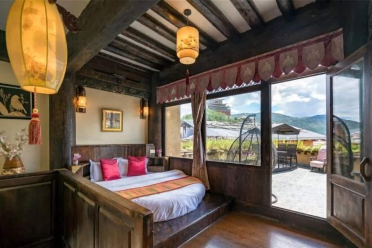 Une chambre avec un grand lit, des poutres apparentes, une fenêtre donnant sur l’extérieur et un luminaire suspendu.