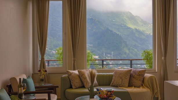 Un salon avec un canapé, une table basse et une vue sur les montagnes, visible à travers de grandes fenêtres.
