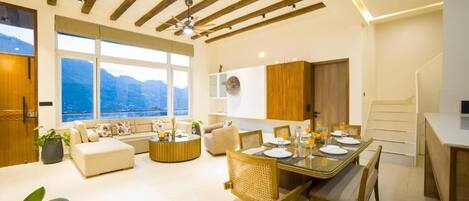 A modern living room with a dining area, large windows, and a view of mountains.