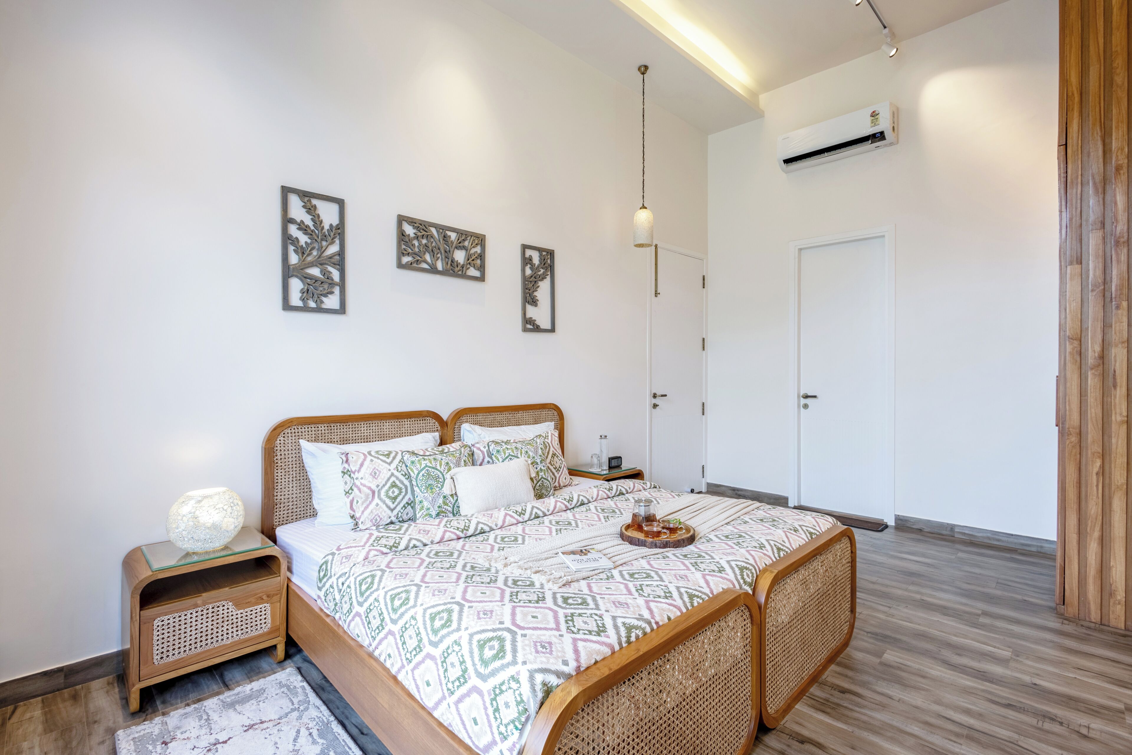 Un dormitorio ordenado con cama, mesitas de noche, una lámpara colgante y aire acondicionado instalado en la pared.