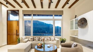 Un salon moderne comprenant un canapé, un fauteuil et une table basse, de grandes fenêtres offrant une vue sur les montagnes et des poutres en bois au plafond.