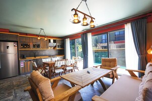 Una cocina moderna con armarios de madera, un comedor con mesa y sillas de madera, y ventanas amplias con cortinas.