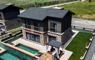 Una casa moderna de dos pisos con piscina, fachada de piedra y ventanas grandes.