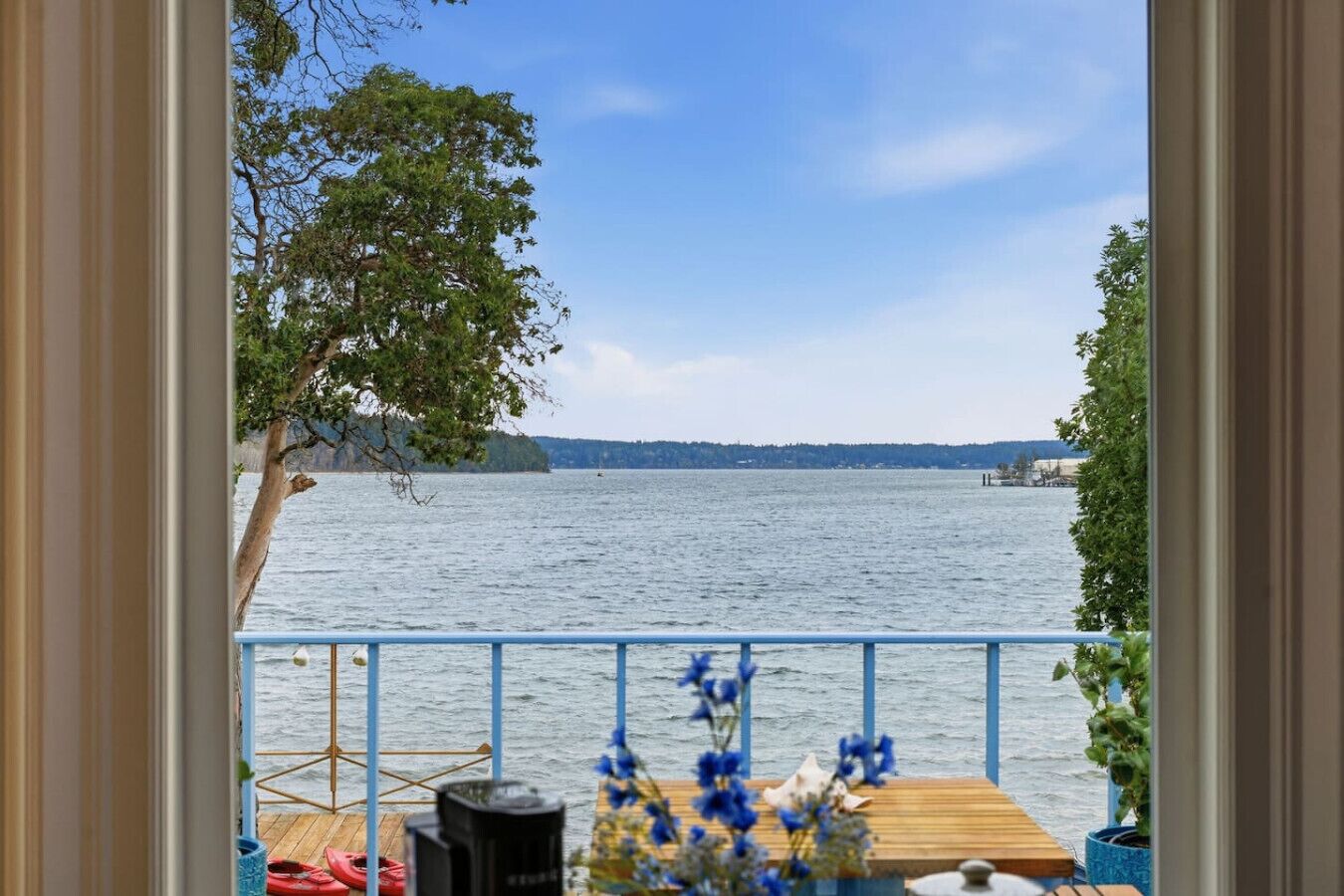 A view from a balcony overlooking a calm lake with a distant shoreline, a wooden deck, and a railing.