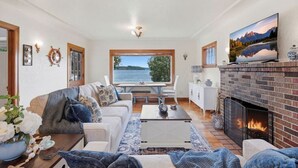 Una sala de estar acogedora con chimenea, comedor y un ventanal con vistas al agua.