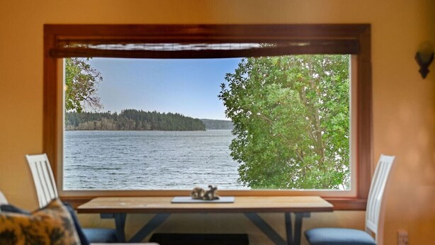 Una habitación con un ventanal grande que da a un lago, una mesa de madera y dos sillas.