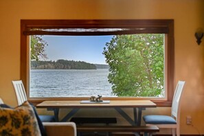 A room with a large window overlooking a lake, a wooden table, and two chairs. - Timeless Tides Cottage | Waterfront, Sauna, Kayaks (Poulsbo)