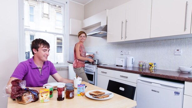 Cozinha com armários brancos, fogão e lava-louças. Há alimentos para o café da manhã no balcão.