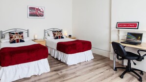 Quarto com duas camas, uma escrivaninha com um laptop e um aviso a indicar 'OXFORD STREET'.