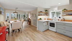 A modern kitchen with built-in appliances, a dining area with a table and chairs, and a living space with a sofa and a coffee table. - The Tide Runner Cottage | Short Walk to Beach + Tandem Kayak (Indianola)