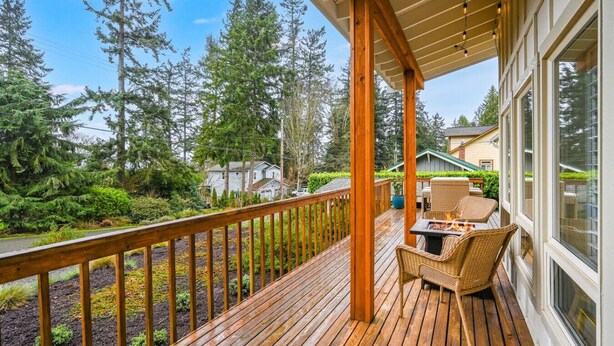 A wooden deck with outdoor furniture, a fire pit, and a view of a forested area. - The Tide Runner Cottage | Short Walk to Beach + Tandem Kayak (Indianola)