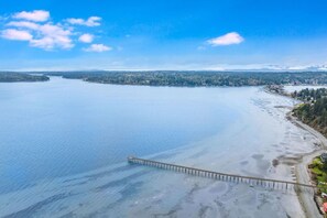Eine Küstenansicht mit einem Steg, der sich in ruhiges Wasser erstreckt, umgeben von bewaldeter Landschaft.