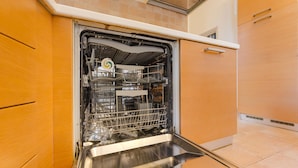 Een open vaatwasser in een keuken met houten kastjes en een betegelde achterwand.