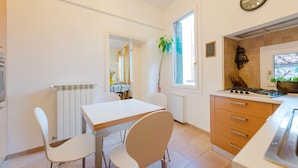 Een keuken met een eettafel, stoelen, een fornuis en een klok aan de muur.