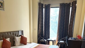 A hotel room with a large bed, a desk, a chair, and a view of the outdoors. - VR RESIDENCY 83 (Gurugram)