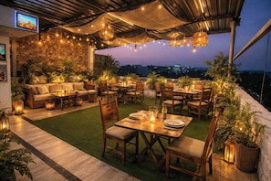 An outdoor patio with a dining area, seating, and a TV screen. - Hotel Dream Connect - Sector 38 (Gurugram)