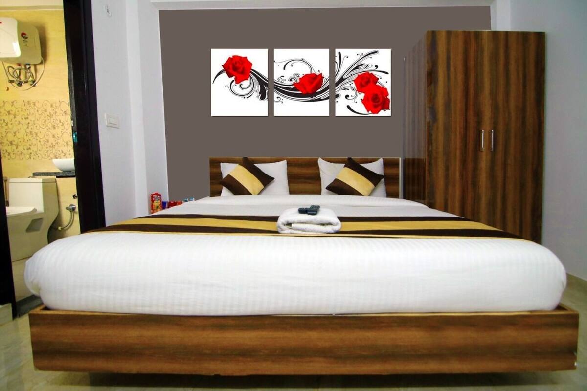A hotel room with a large bed, a wooden headboard, a wardrobe, and a wall with three red rose paintings.