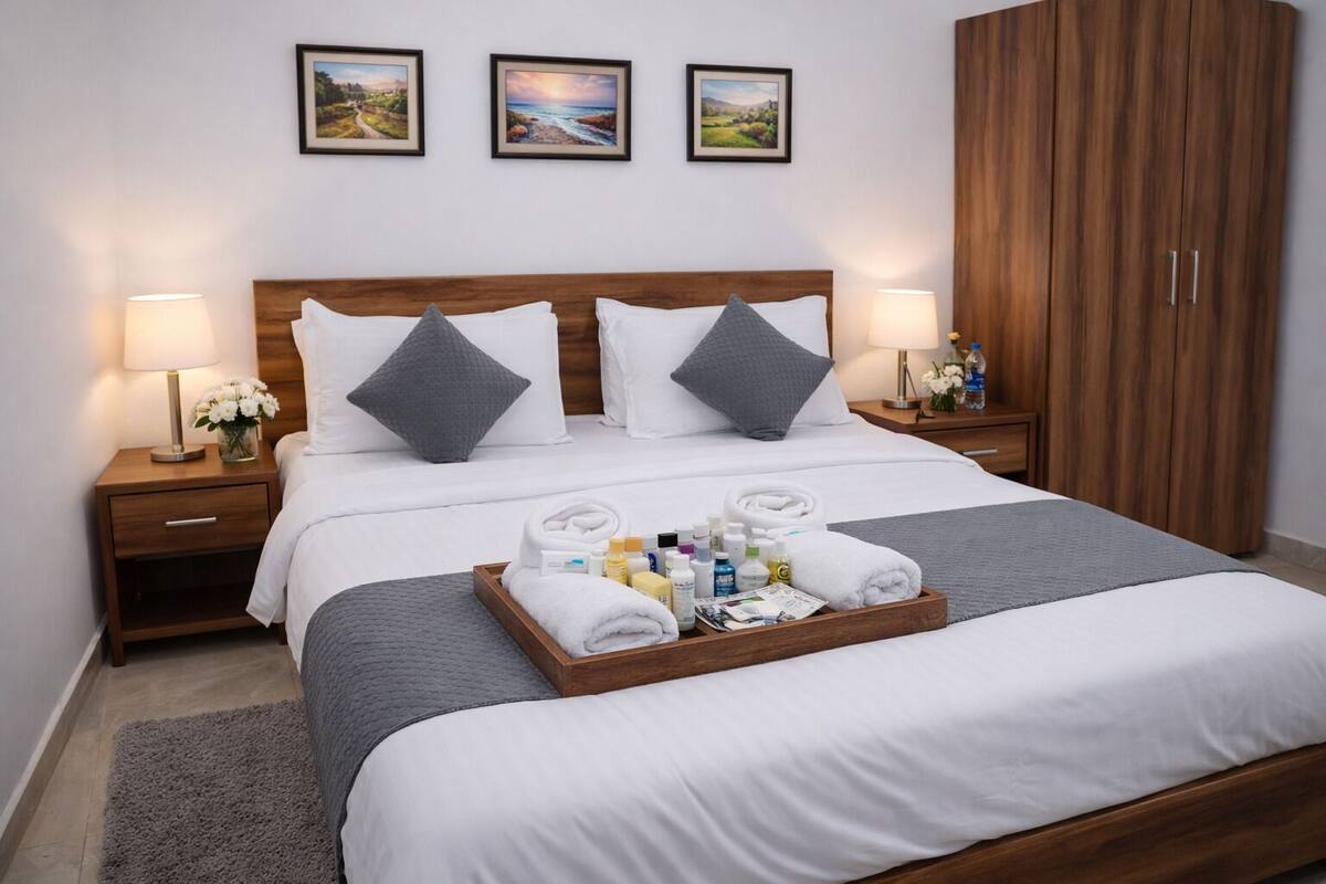 A hotel room with a wooden bed, grey bedding, a tray of toiletries, and framed pictures on the wall.