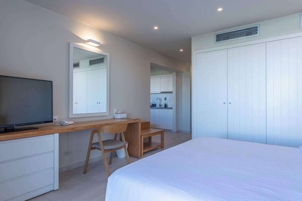 A modern bedroom with a bed, a desk with a chair, a television, and a wardrobe.