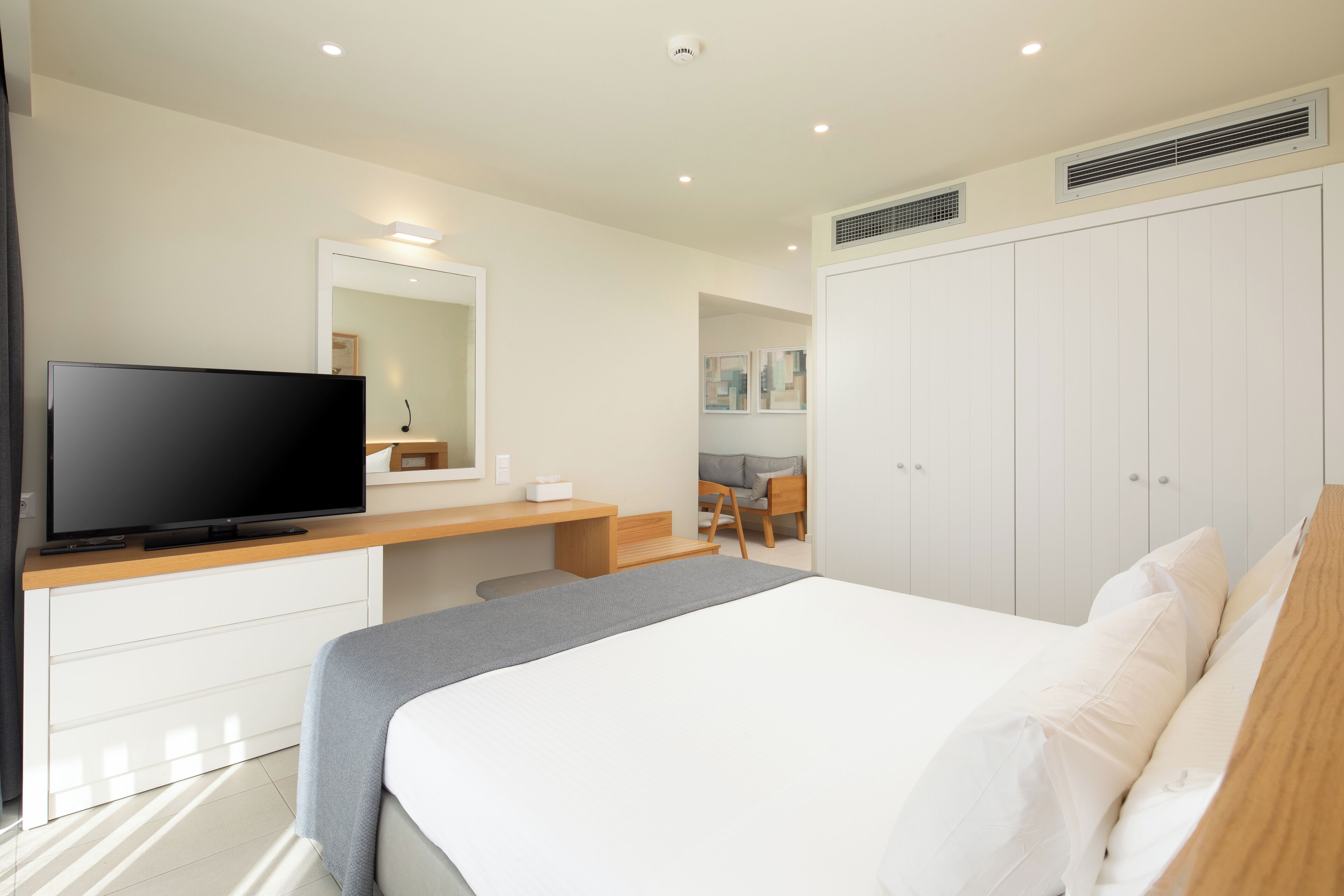 A modern hotel room with a bed, a TV, a desk, and a wardrobe.