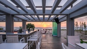 A covered outdoor seating area with tables and chairs, a view of the beach, and a sunset. - Thalassa Suites Corfu (Corfu)