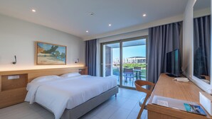 A hotel room with a bed, a desk with a chair, a television, and a painting on the wall. - Thalassa Suites Corfu (Corfu)
