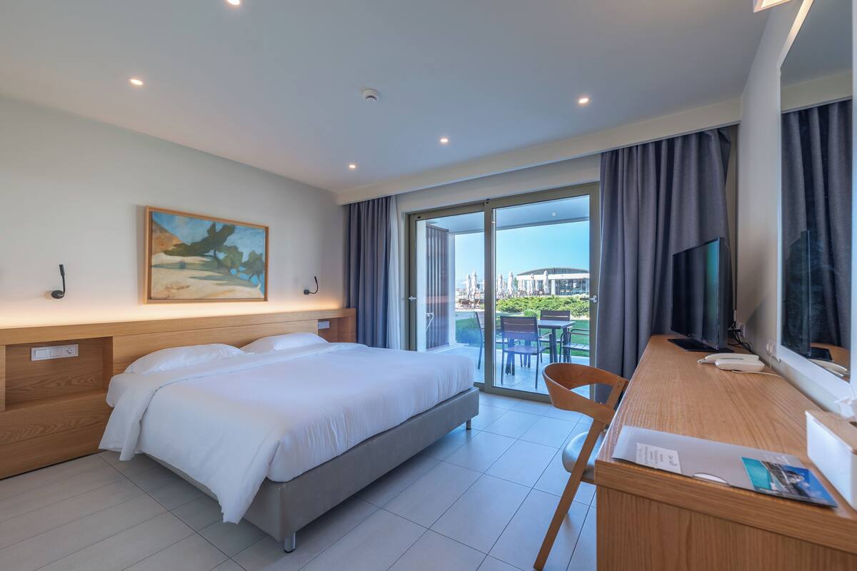 A hotel room with a bed, a desk with a chair, a television, and a painting on the wall.