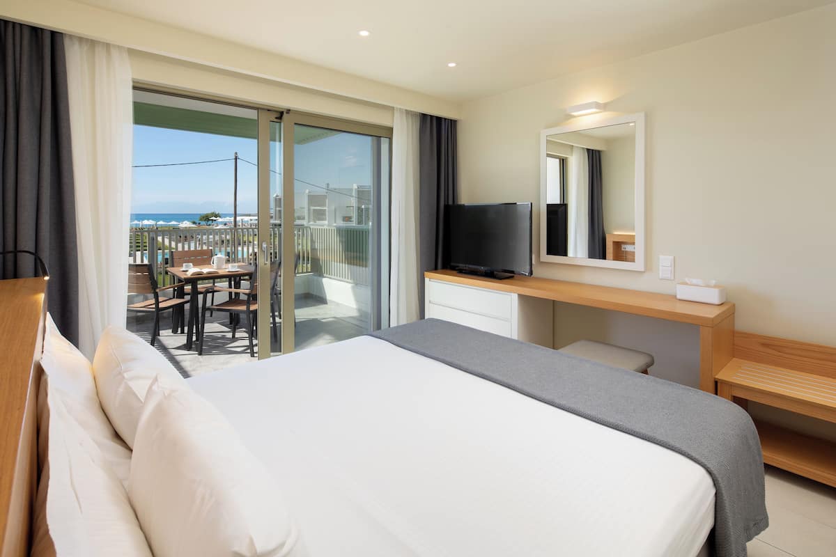 A hotel room with a bed, a desk, a television, and a balcony with a view.