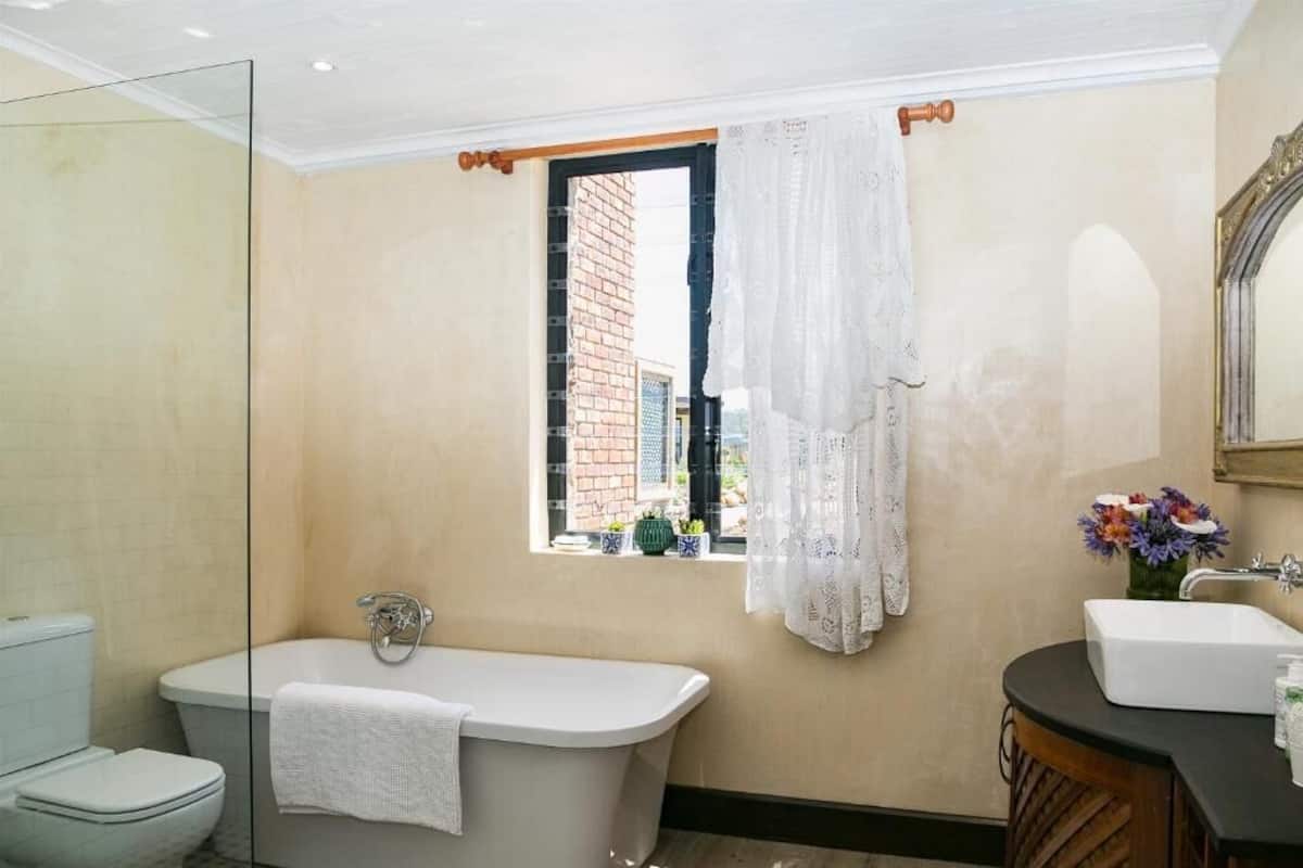 A bathroom with a bathtub, toilet, and sink, a window with a curtain, and a mirror.