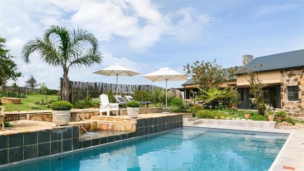 A swimming pool with lounge chairs, umbrellas, and a stone building in the background. - Narnia Luxury Self Catering Guest House (Knysna)