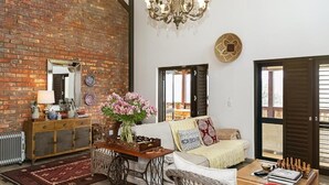 A living room with a brick wall, a chandelier, a sofa, a coffee table, and a chessboard. - Narnia Luxury Self Catering Guest House (Knysna)