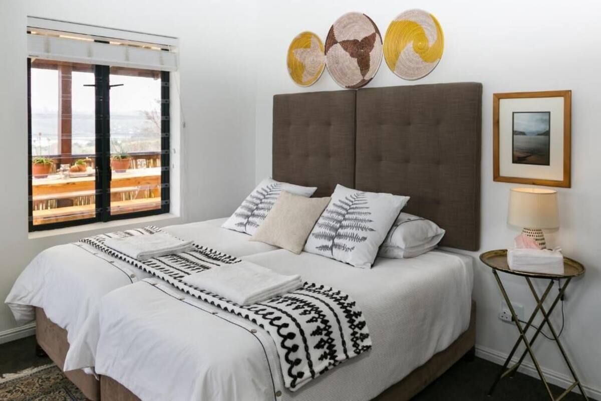 A bedroom with a large bed, a window with a view, decorative wall art, and a bedside table with a lamp.