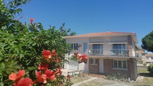 A two-story house with a balcony, surrounded by greenery and flowering plants. - GRANDE VILLA PROCHE MER WIFI PARKING (Agde)