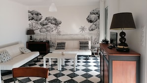 A living room with a checkered floor, a sofa with patterned cushions, a coffee table, a lamp, and a wall mural. - GRANDE VILLA PROCHE MER WIFI PARKING (Agde)