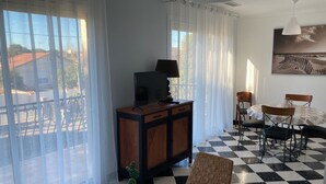 A room with a checkered floor, a dining table with chairs, a television on a wooden cabinet, and a potted plant. - GRANDE VILLA PROCHE MER WIFI PARKING (Agde)