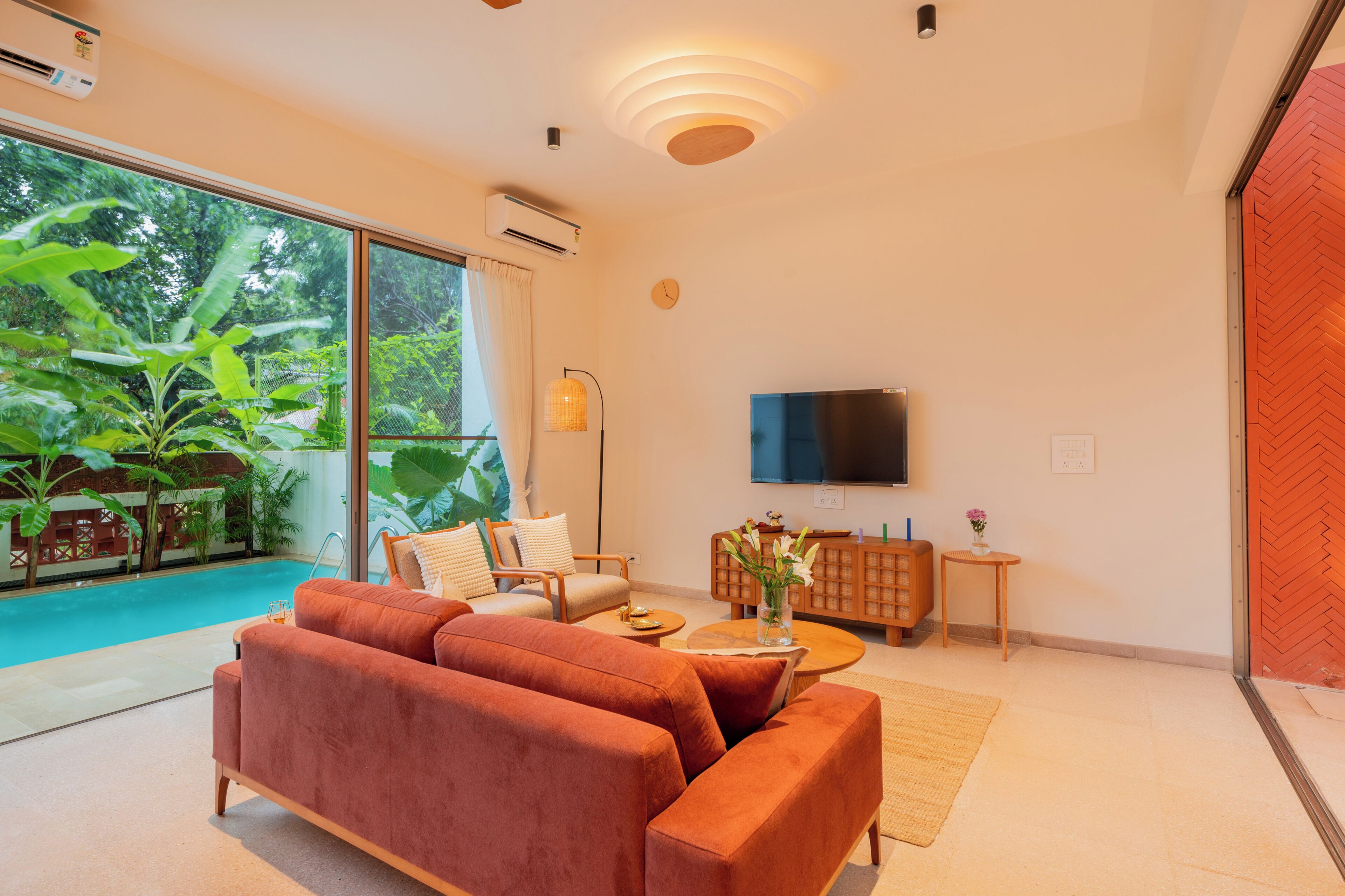 Un salon moderne avec un canapé, un téléviseur et une vue sur une piscine et un espace verdoyant.